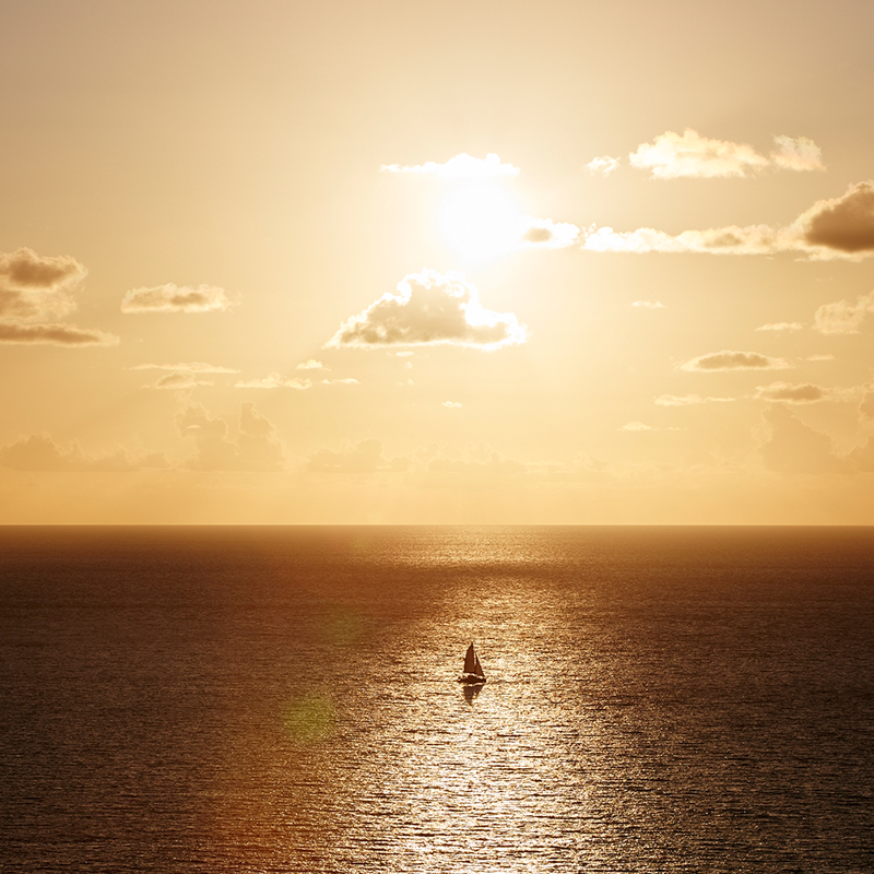 A sailboat in the Atlantic ocean in front of a golden sunset